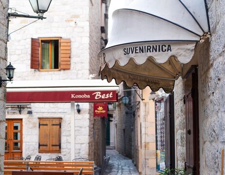 Enge steinerne Gasse mit einer Markise des Suvenirnica-Ladens und Sitzgelegenheiten im Freien vor der Konoba Best.