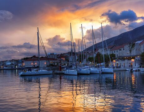 Segelboote in einem Jachthafen mit farbenfrohem Himmel bei Sonnenuntergang und Spiegelungen auf dem Wasser.